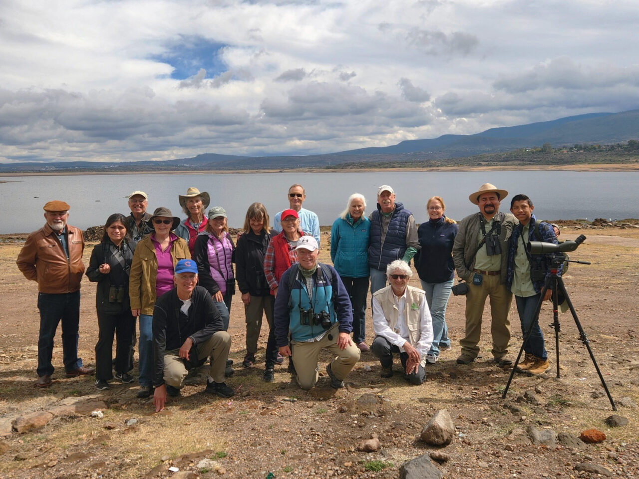 A group of birdwatchers stands at the edge of a lake.