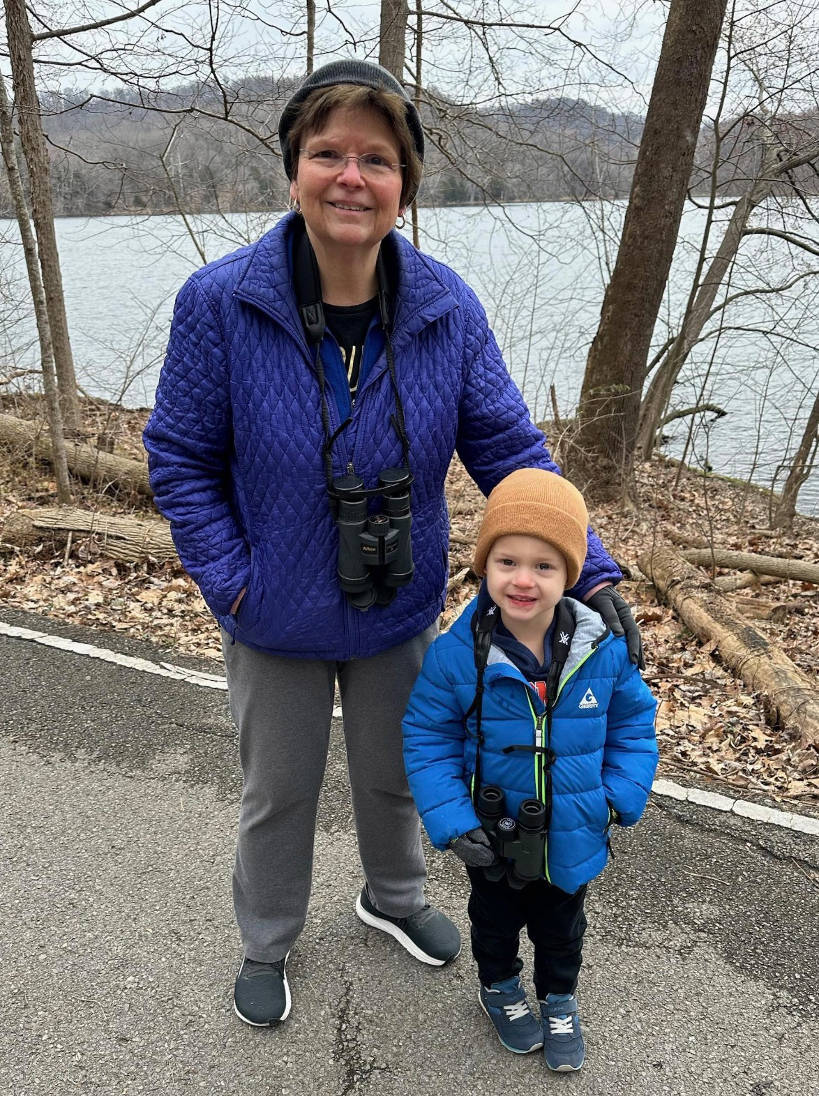 A woman and a child stand near the edge of a lake.