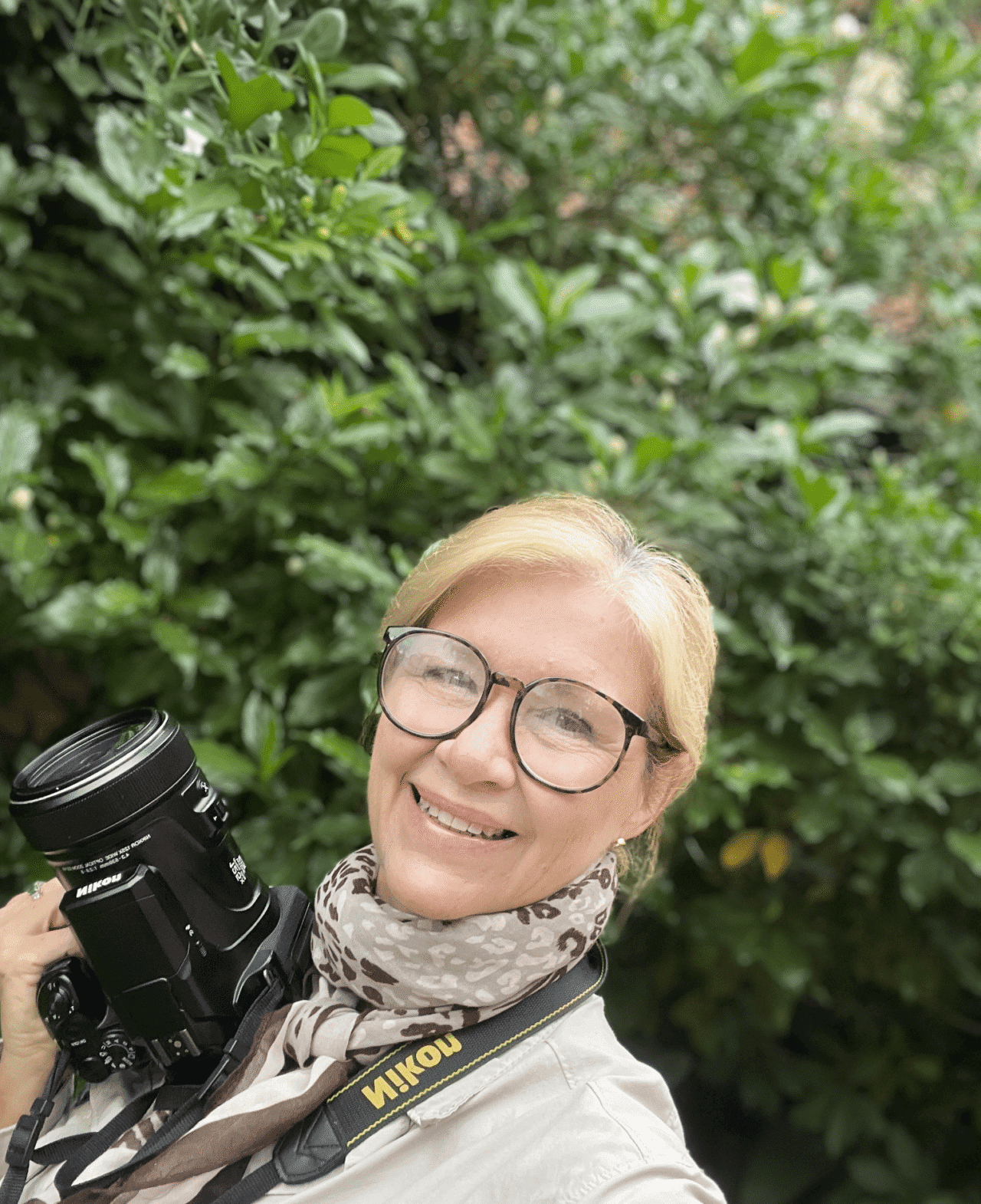 A smiling person with birdwatching equipment.