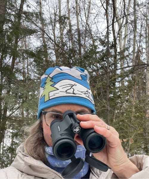 A person smiling and holding binoculars.