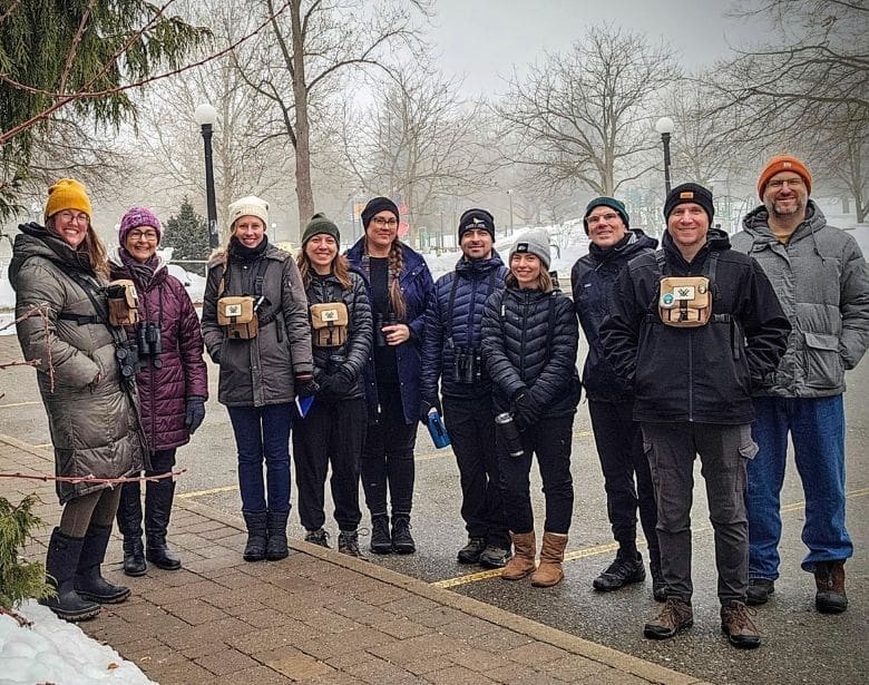 A group of smiling people with birdwatching equipment.