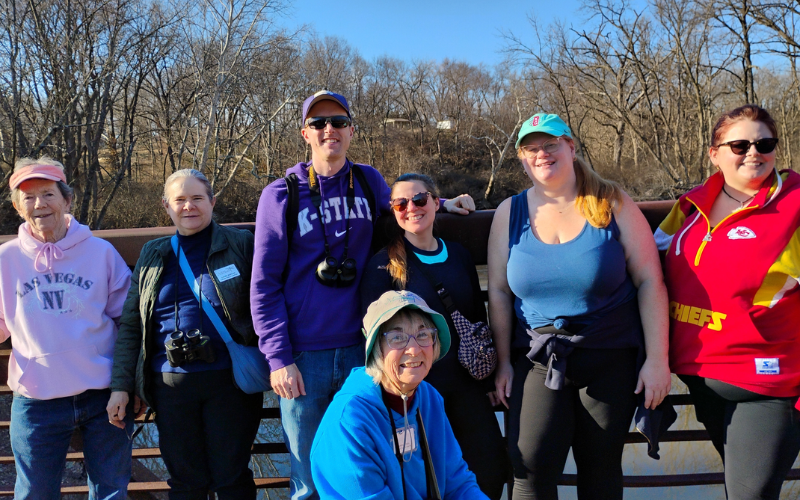 A smiling group of people with birdwatching equipment.