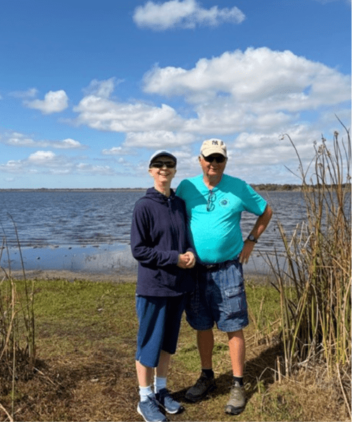 Two people smiling in front of a body of water.