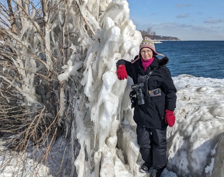 A person with binoculars, smiling while leaning on ice.