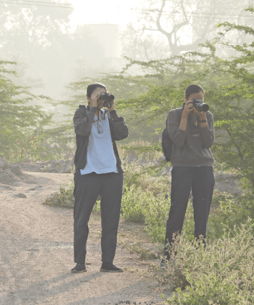 Two people birdwatching with a pair of binoculars and a camera.