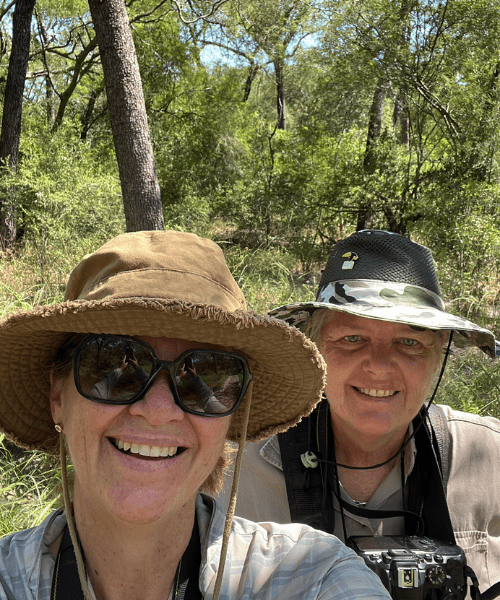 Two smiling people in a sunny wooded area.