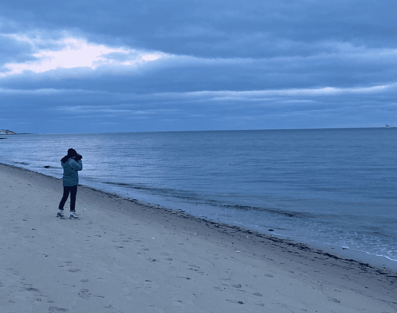 A person birdwatching with binoculars at the beach.