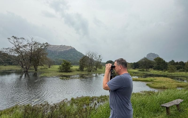 A person using binoculars to birdwatch in front of a body of water. 
