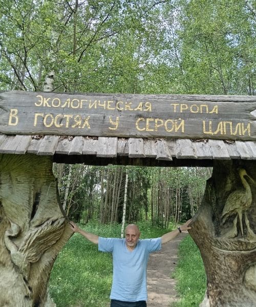 A person smiling under a wooden sign.