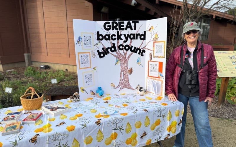 A person smiling while standing next to a trifold with the words "Great Backyard Bird Count" written.