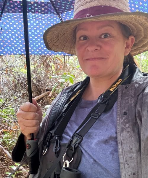 A person smiling with binoculars while holding an umbrella.