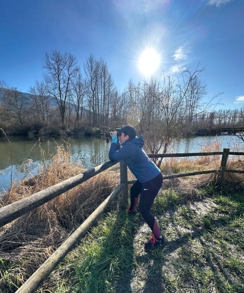A person birdwatching in front of a river.