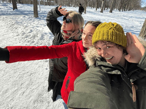Three smiling people in a snowy wooded area.